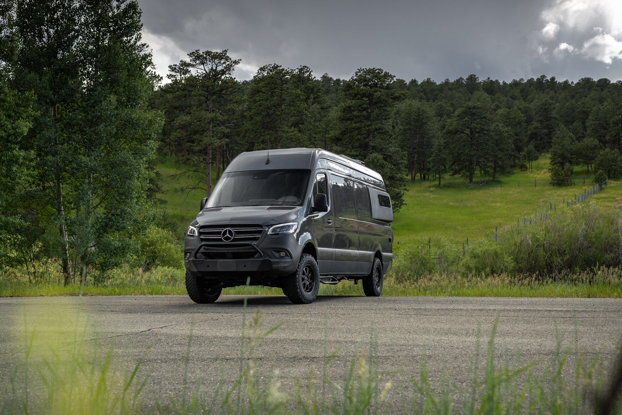 Black Mercedes-Benz van on a road with trees in the background