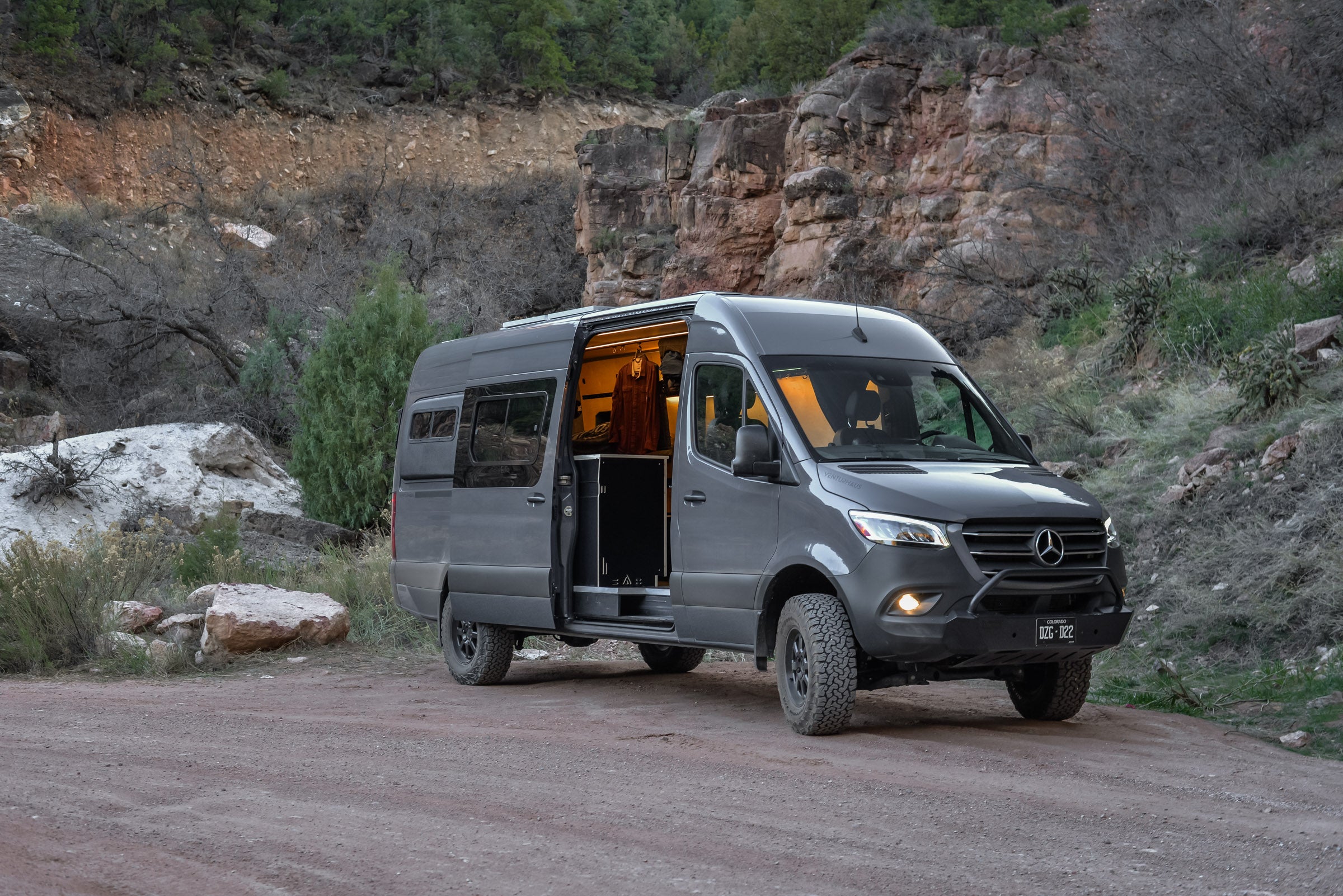Gray Mercedes-Benz van with open door on a dirt road in a rocky landscape
