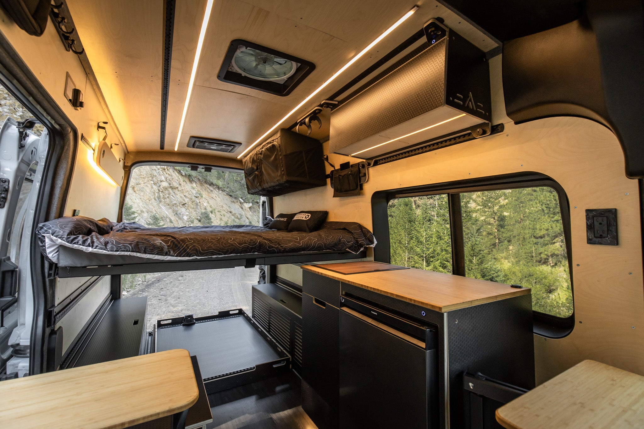 Interior of a camper van with the Venturhaus Modular Van System including a sleeping area, kitchenette, and window view