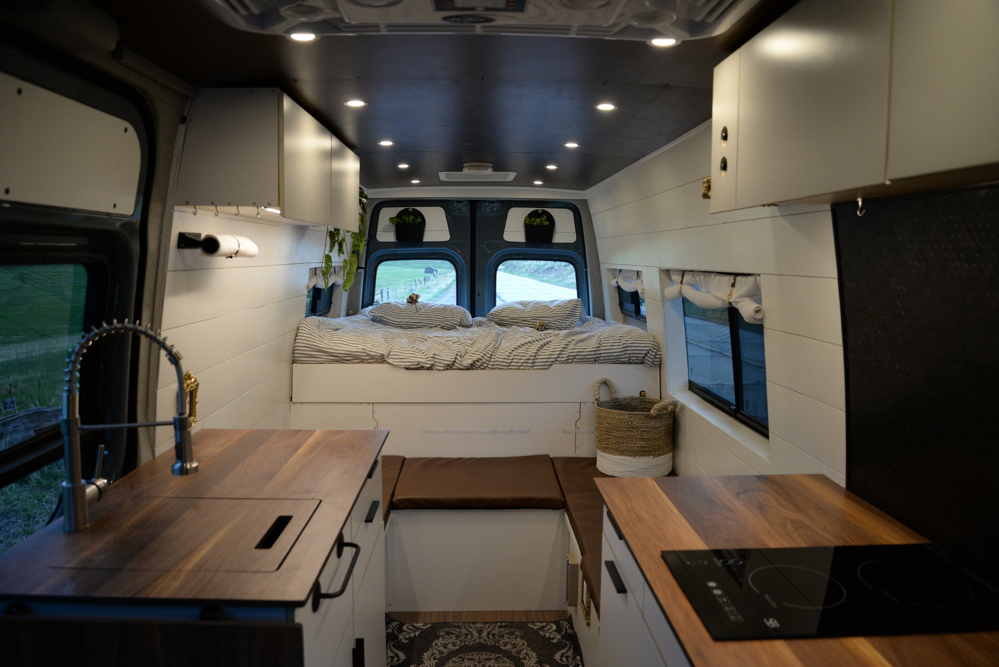 Bespoke van conversion with a kitchen setup, bed, and windows.