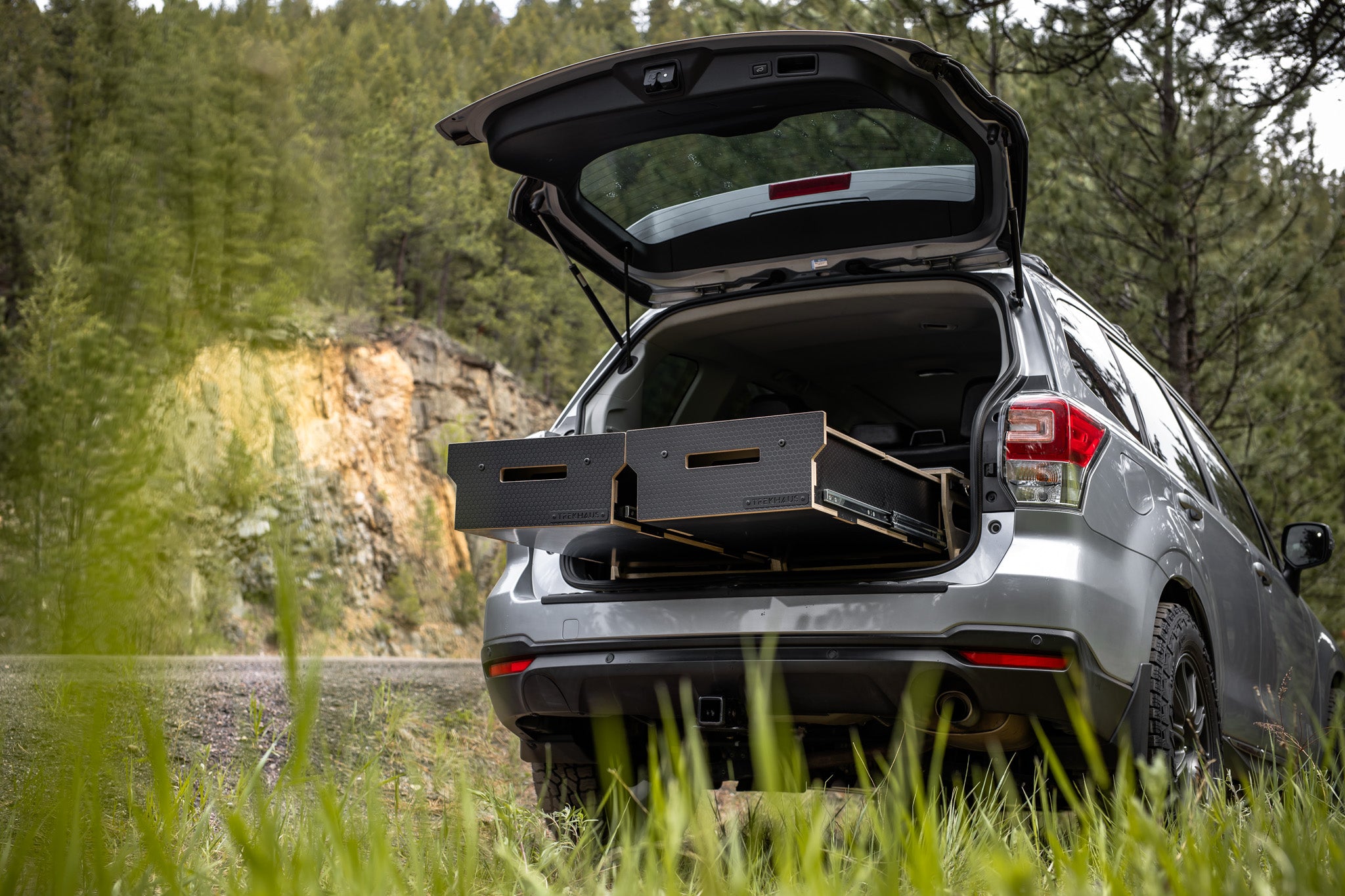 Silver SUV with open trunk in a forest setting with a Trekhaus SUV Camper System storage drawers open