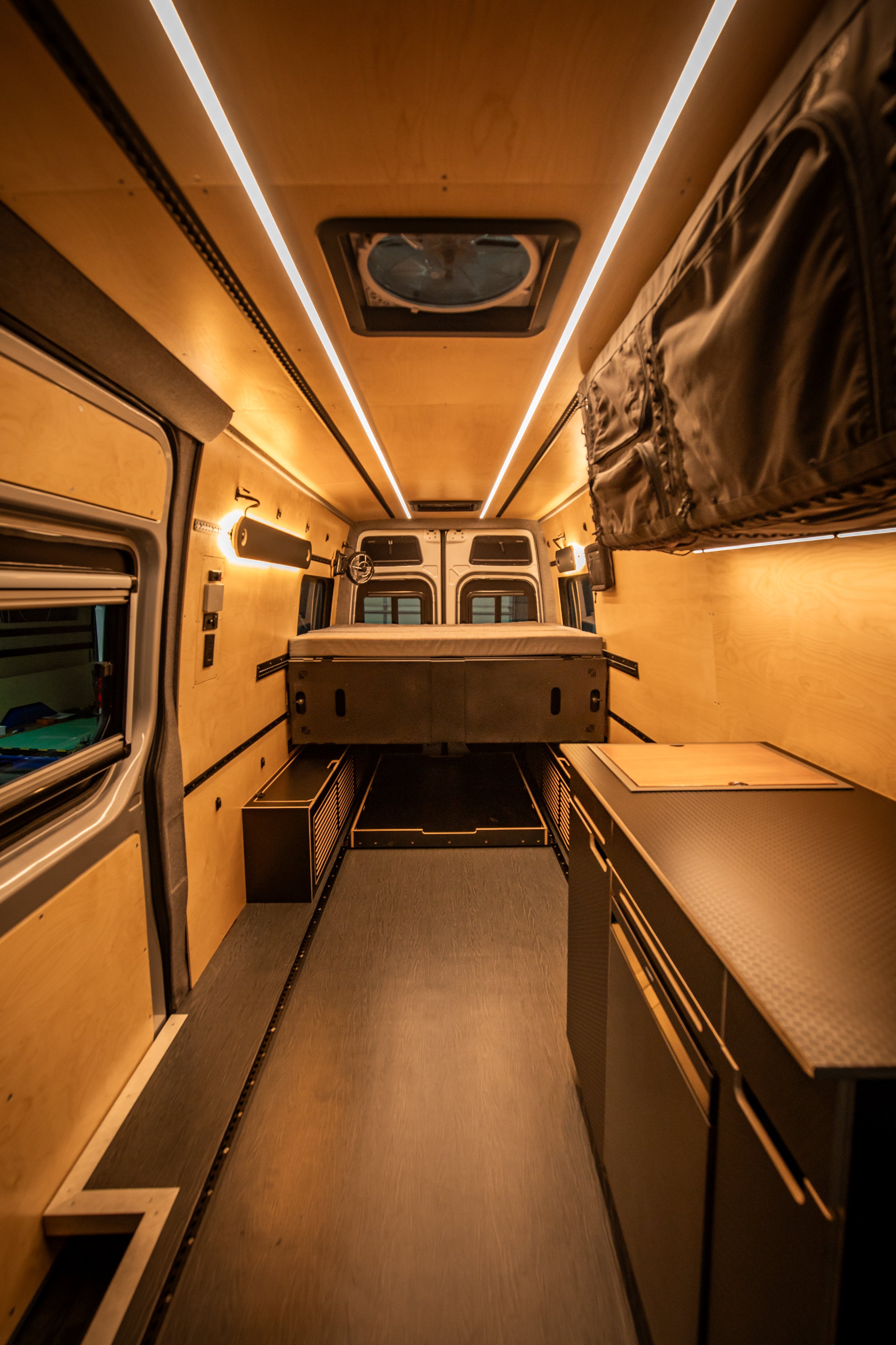 Compact living space inside a van with the Venturhaus Modular Van system, including a bed, kitchenette, and storage area.